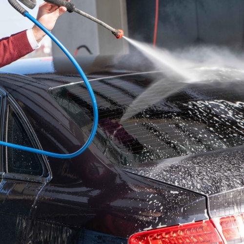 Bilvask udført af en mand med vandslange der sprayer sæbe af bilen.